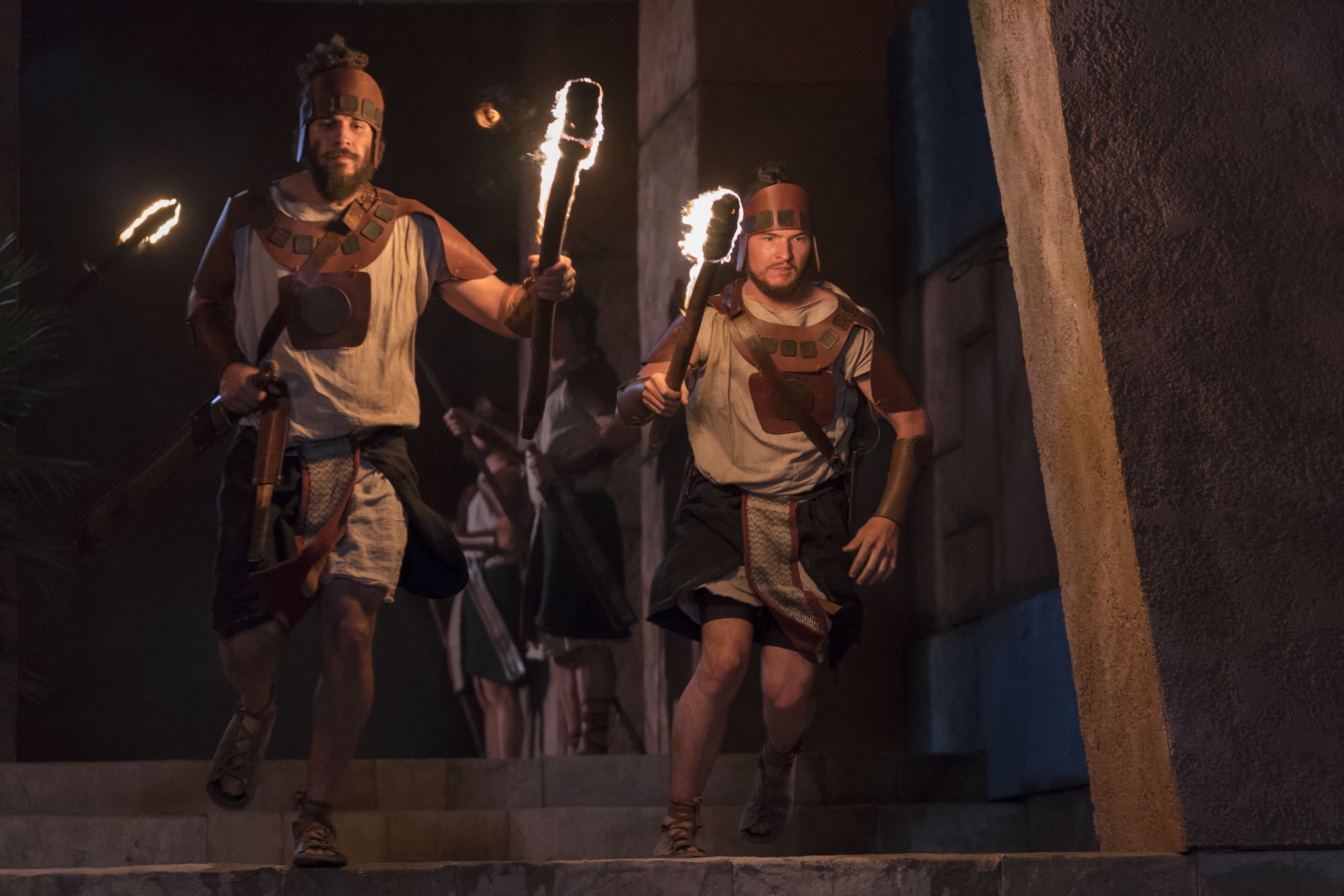 King Noah's guards run down a hall with torches in their hands.