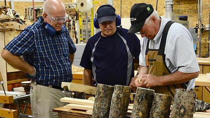 Three older men in a workshop cutting through wood.