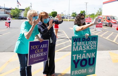 Relief Society General Presidency members hold signs and wave to volunteers as they donate masks