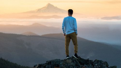 A man stands on the top of a mountain and looks off into the distance.