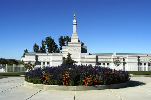 A flower bed full of orange and purple flowers, with the Bismarck North Dakota Temple in the background.