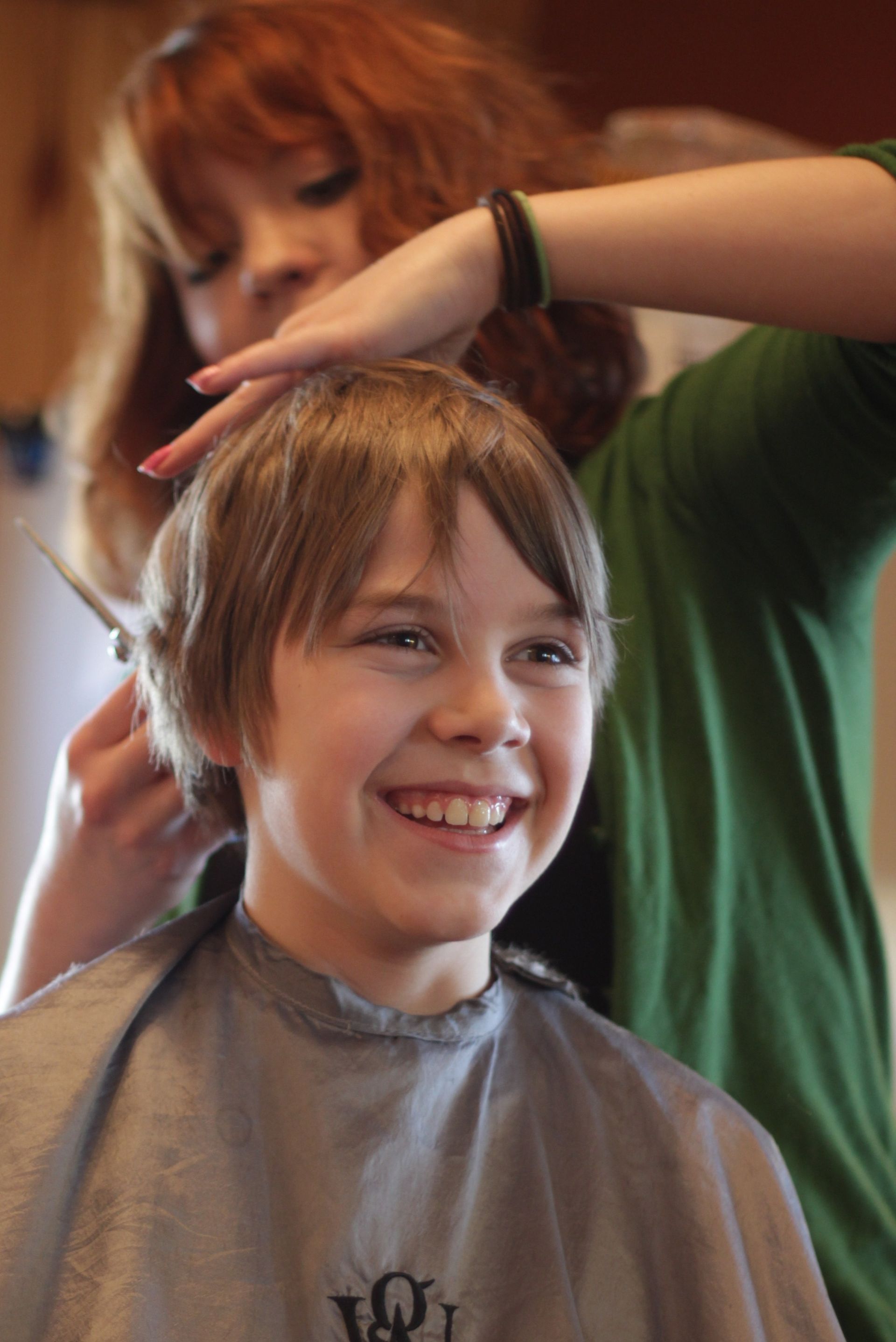 A woman helps cut a young boy’s hair.