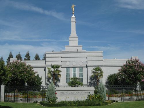 A view of the Fresno California Temple, with the temple’s granite sign in the foreground and green trees on the temple grounds.