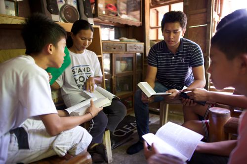 Ministering brothers sitting in a circle with a family and reading the scriptures together in the Philippines.