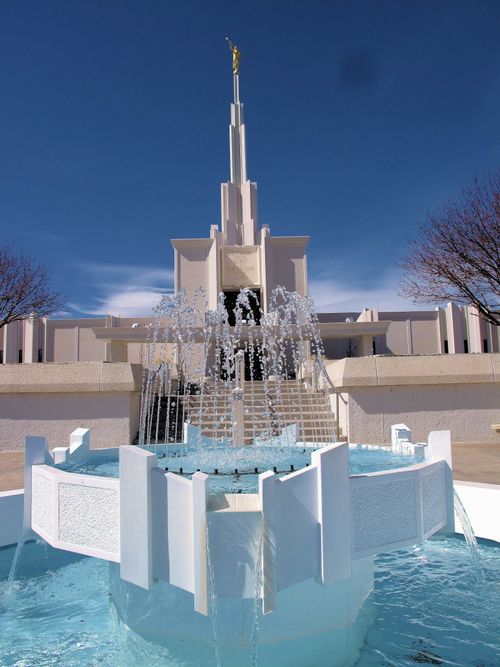 The fountain at the front entrance to the Denver Colorado Temple, with the temple seen in the background against a deep blue sky.