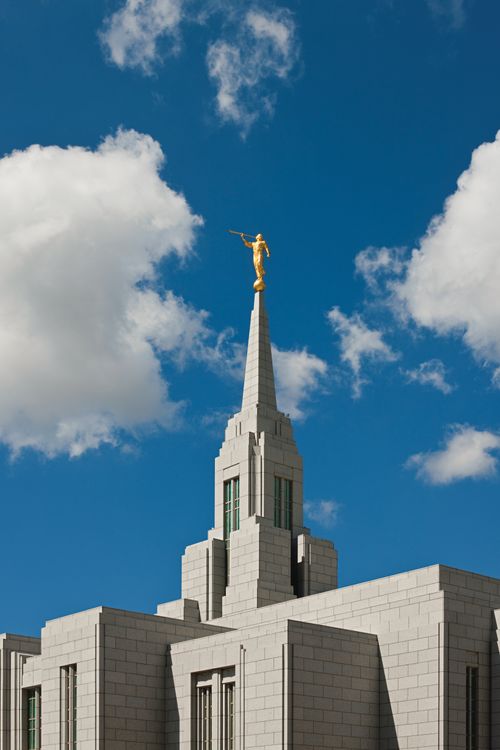 The top half of the Cebu City Philippines Temple, with the spire and angel Moroni set in front of a blue sky with several white clouds.