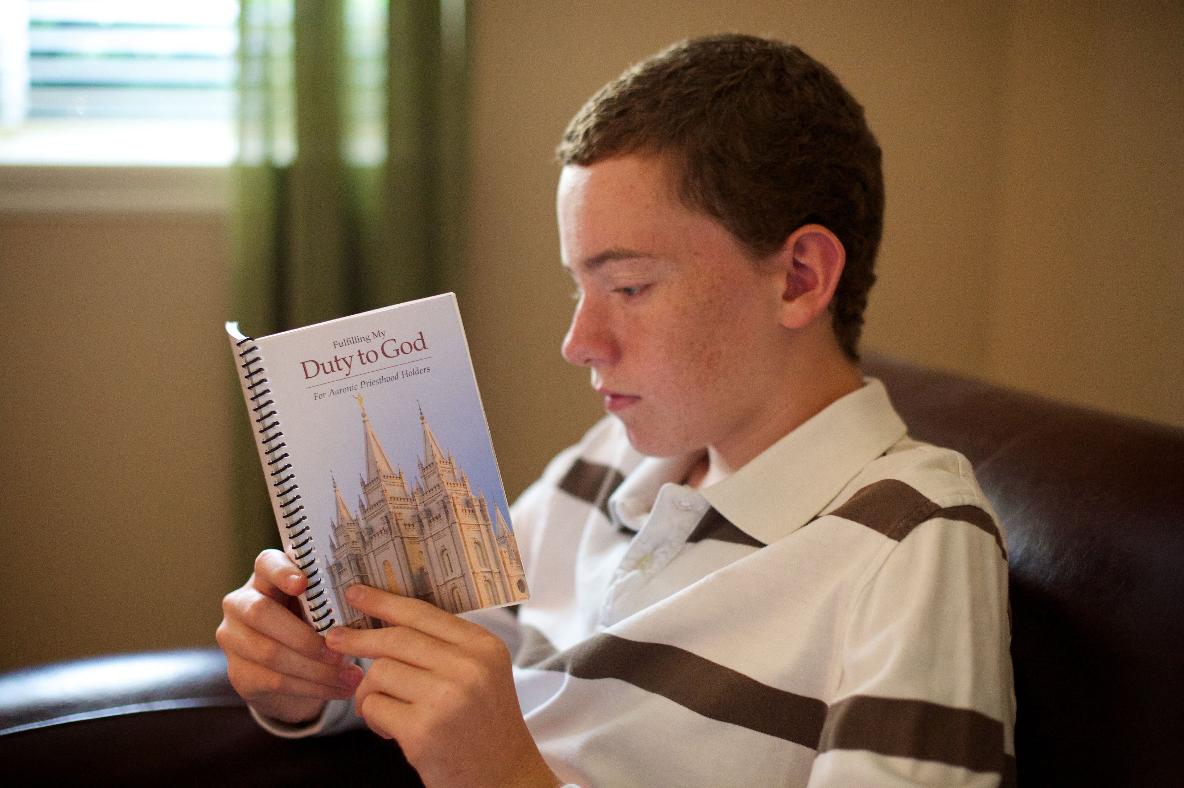 A young man sits in an armchair and reads from the booklet Fulfilling My Duty to God.