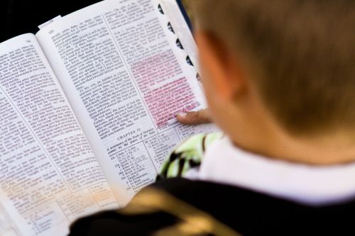 A boy holding a copy of the Book of Mormon open to Moroni chapter 10, which has several verses marked in red.