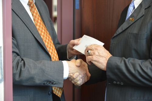 people shaking hands while one passes an envelope to the other