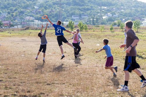 A young man jumps into the air to catch a Frisbee as a group of boys and girls run after him.