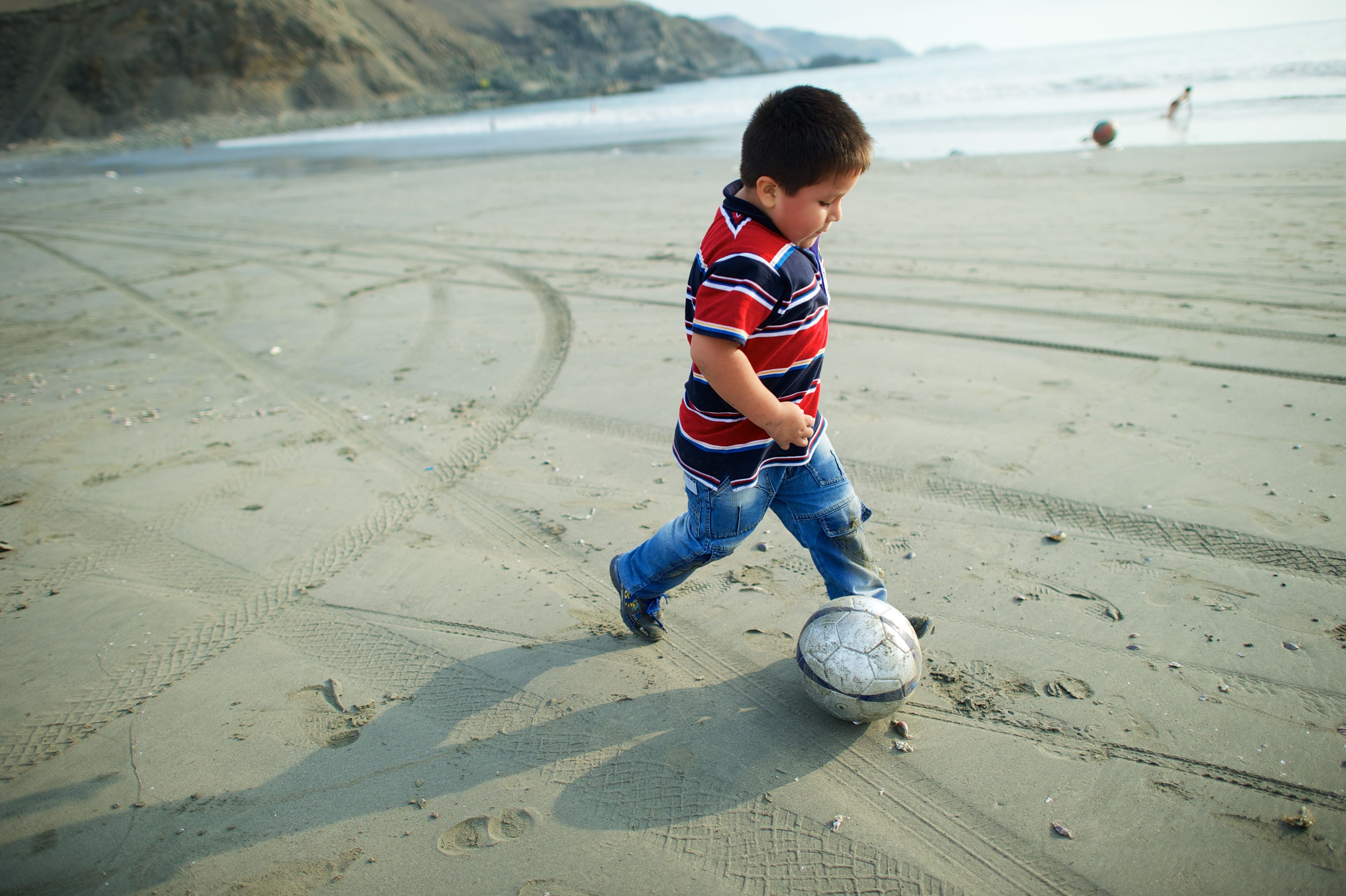 A young Peruvian boy plays soccer on the sand.