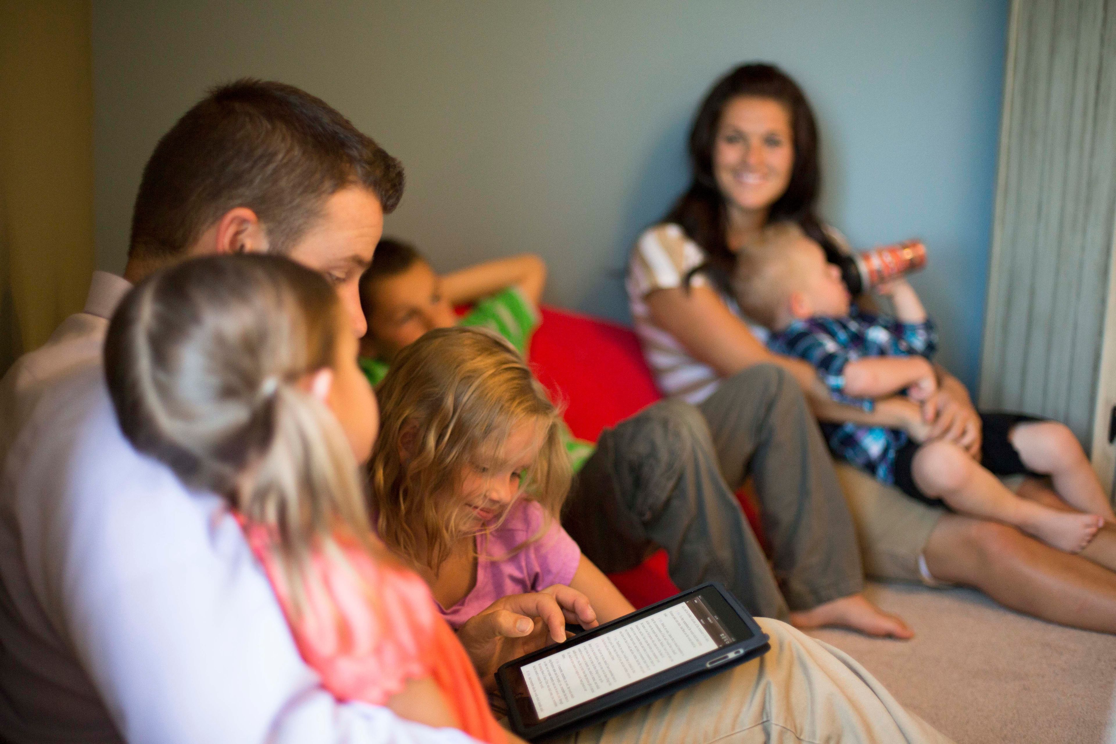 A family sitting down together while the father reads from a tablet.  