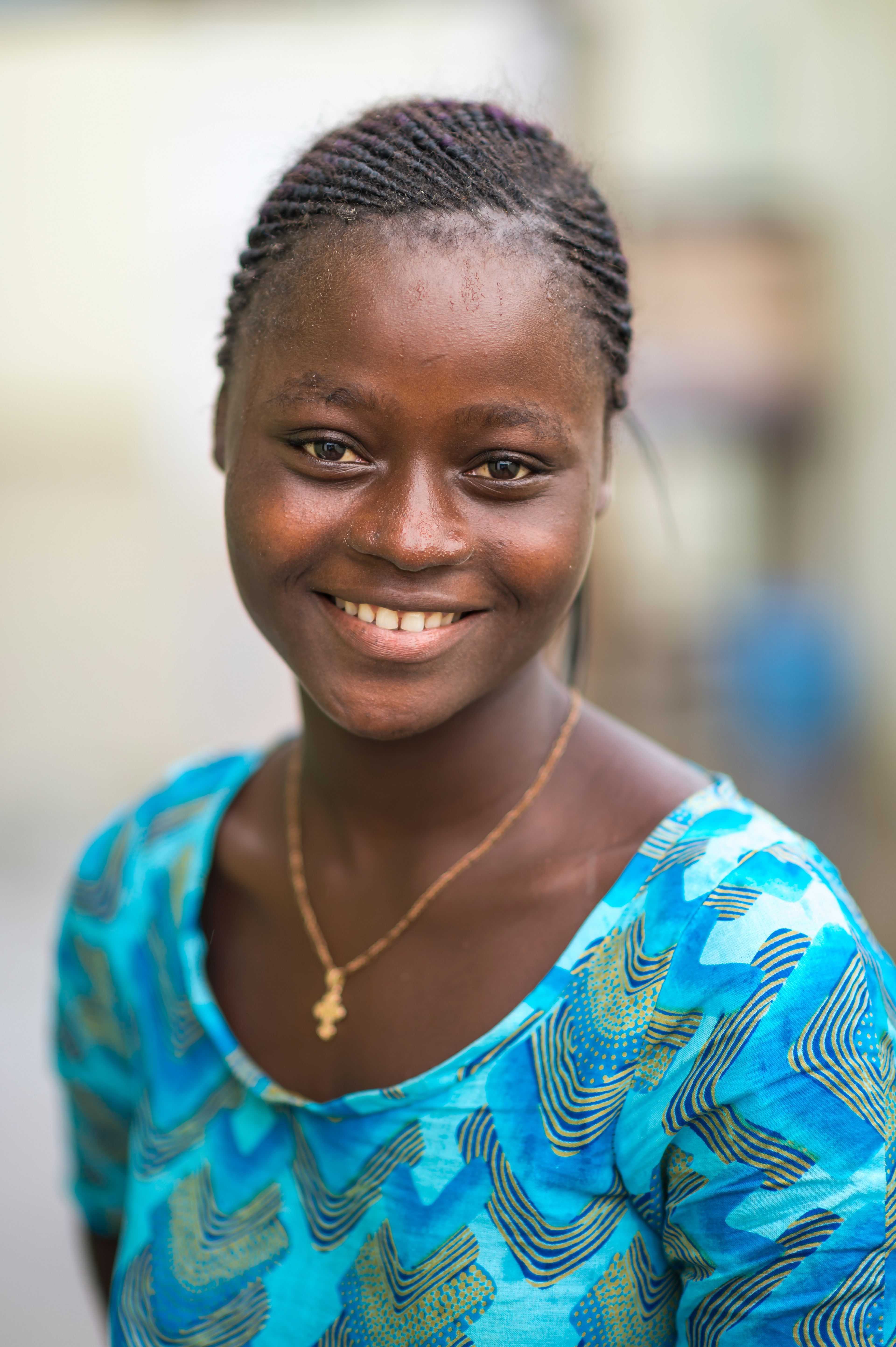 A portrait of a young woman in Ghana, wearing a blue shirt, smiling.