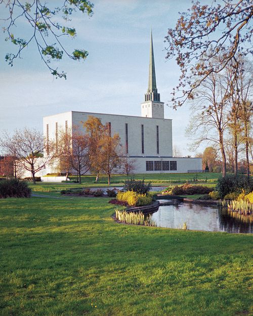 A side view of the London England Temple on a fall day, with the temple grounds and pond in the foreground.