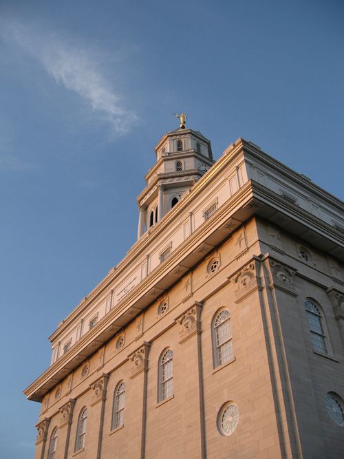 The front of the Nauvoo Illinois Temple from below, with the spire against a blue sky.