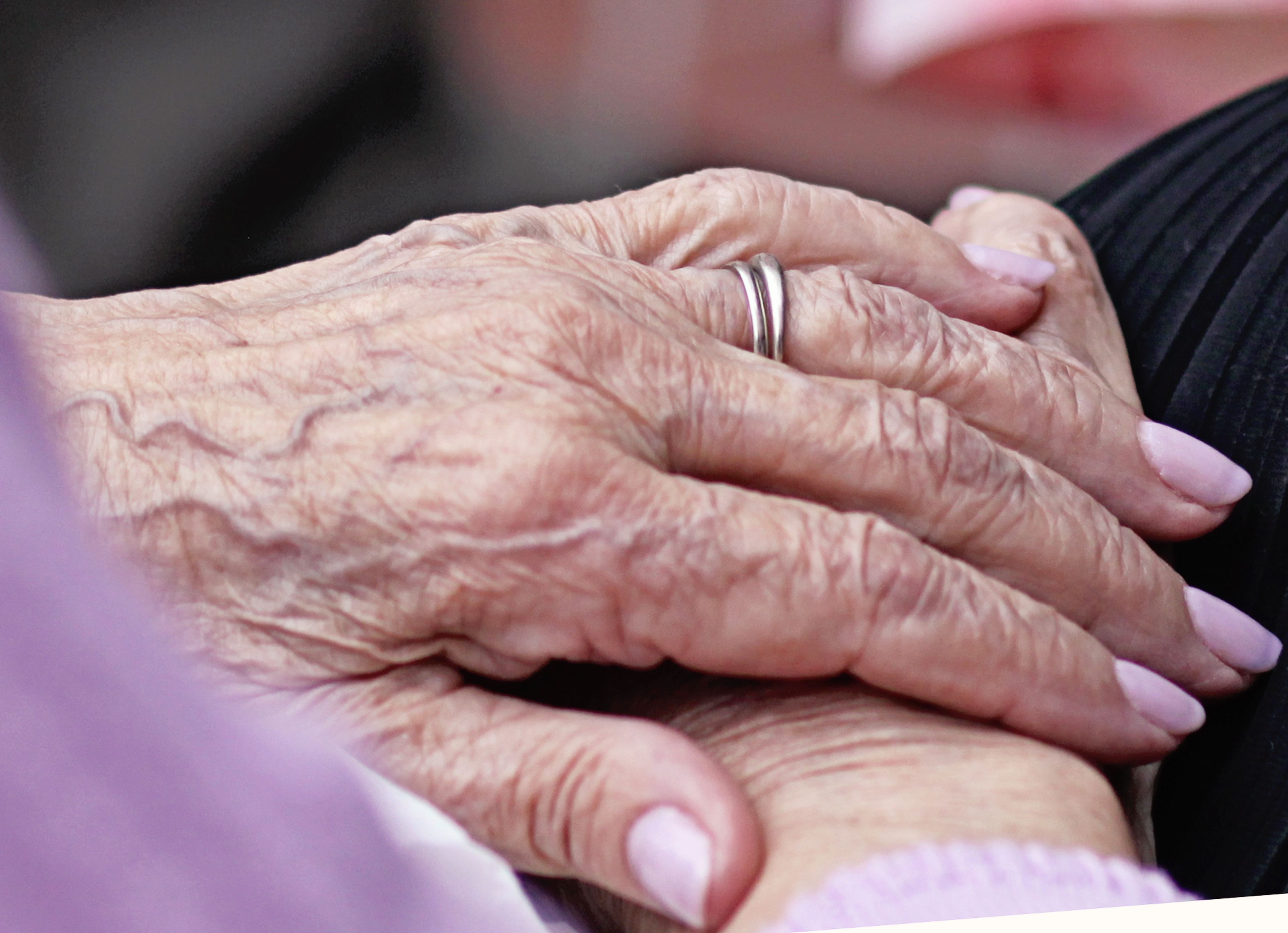 An elderly woman’s hand with a silver wedding band.