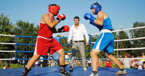 Two men in a park boxing in a boxing ring with a man acting as Referee.