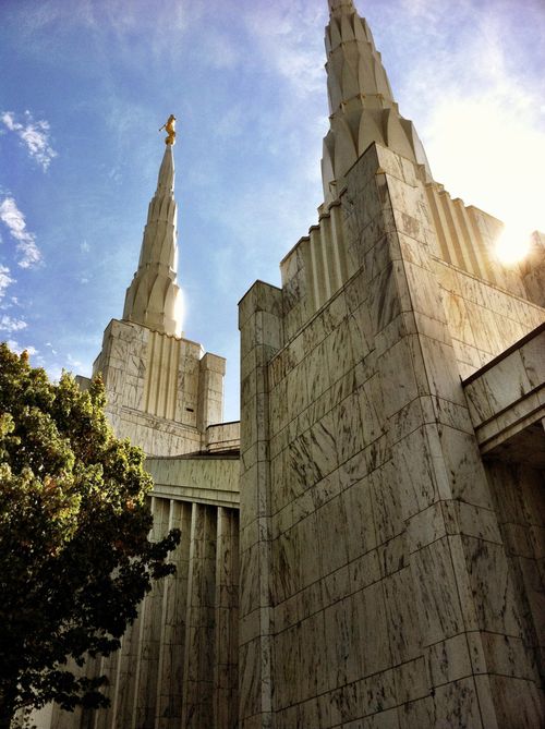 Some of the spires on the Portland Oregon Temple, with a ray of sun lighting up the right side and a green tree showing on the left.