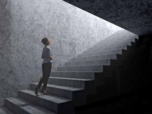 woman climbs stairs going from darkness to light