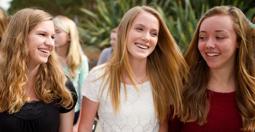 Young women walking together.  They are smiling and laughing.  They are dressed in Sunday clothes.