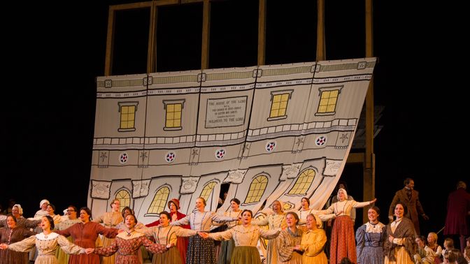 A group of performers dressed in pioneer clothing on a stage in front of a temple set piece.