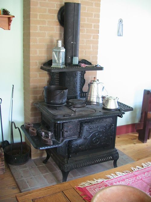 A large black cast-iron stove with silver pots in a room with a wooden floor and bricks in the wall.
