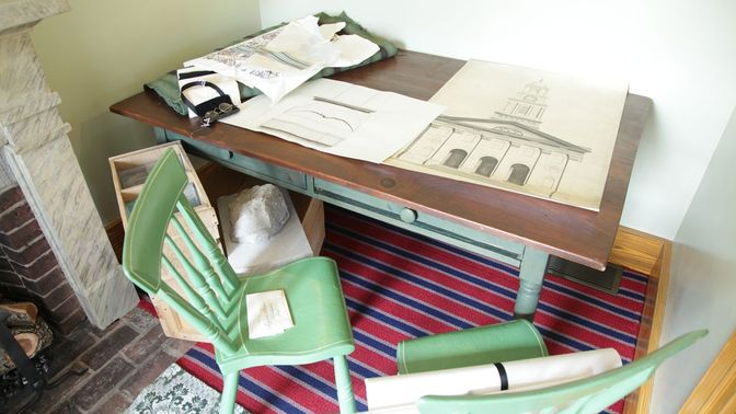 Two green chairs in front of a desk with architectural drawings spread out on it.