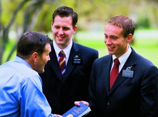 two elder missionaries giving man a Book of Mormon