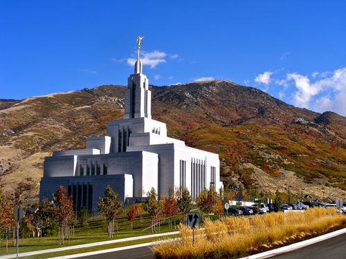 The Draper Utah Temple seen from across the street on an autumn day, with a row of trees in the temple’s parking lot.