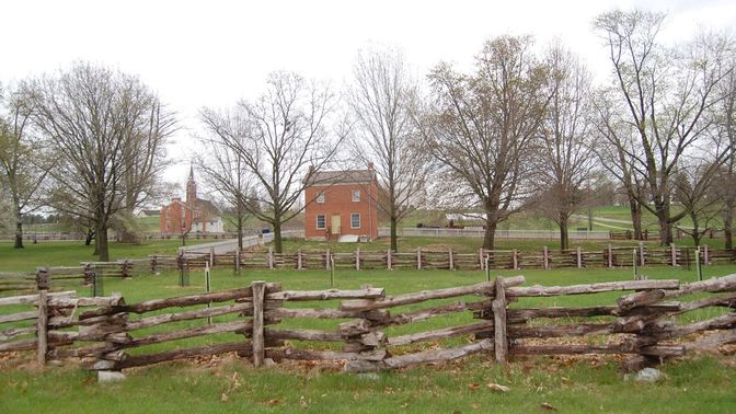 Split rail fence surrounding a half lot with trees and a brick home in the background.