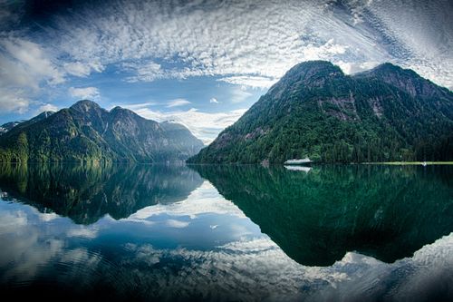 Mountains and clouds in an Alaskan lake with a boat in the water.