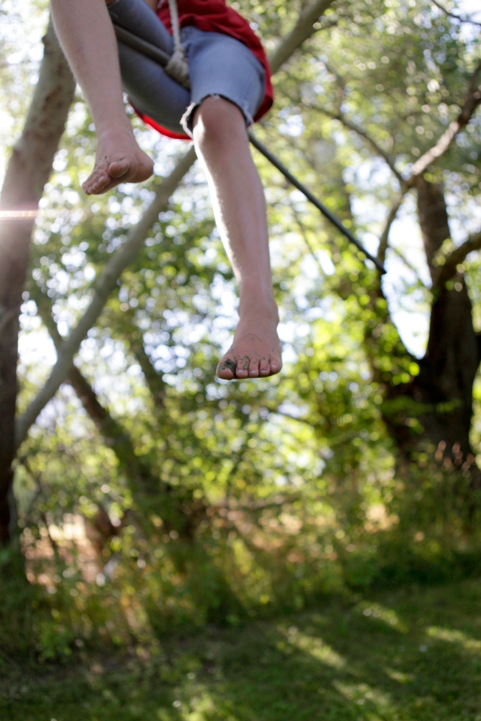 A child hangs on a rope swing outside.