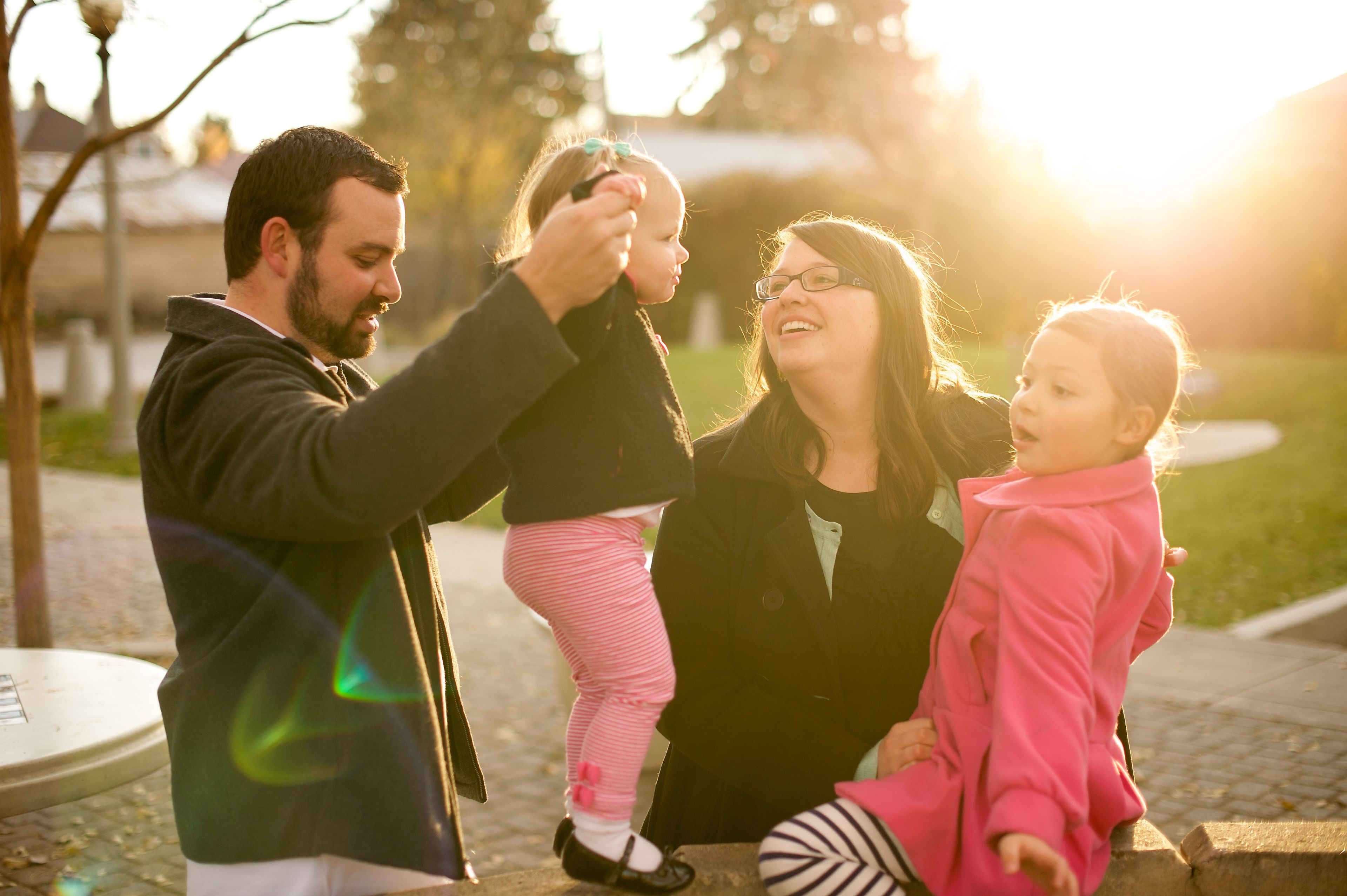 A mother and father play with their two daughters outside.