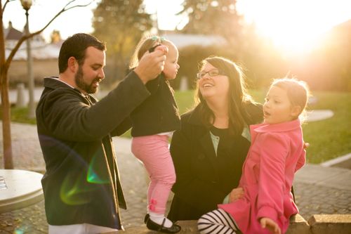 A mother and father play with their two daughters outside at sunset.