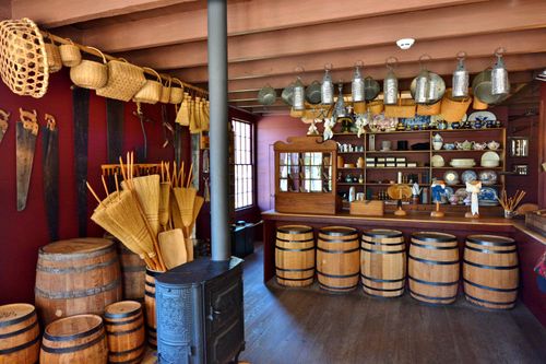 A small wooden store filled with goods from the pioneer era, such as barrels, brooms, saws, pots, and pans.
