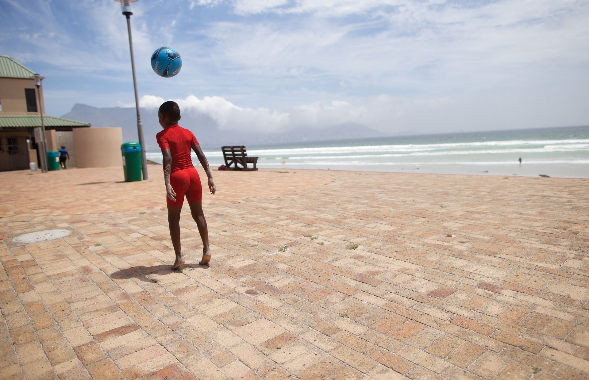 Tendai lässt einen Ball an seinem Kopf abprallen. Auf dieser Terrasse in Strandnähe hat er jede Menge Platz, um seine Fußballkünste zu vervollkommnen. In der Ferne ist der Tafelberg, ein Wahrzeichen Kapstadts, zu sehen.