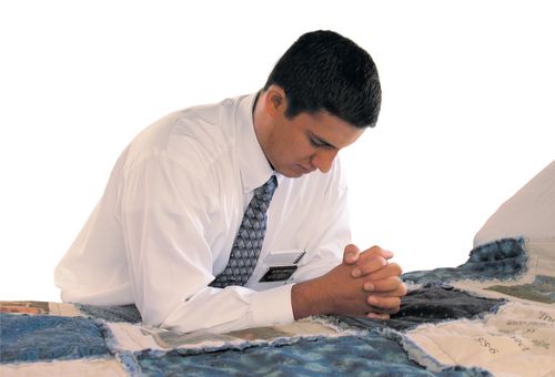 An elder missionary kneelining at his bed praying.