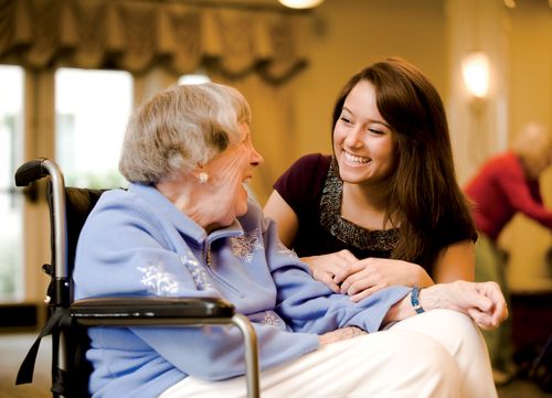 A young woman visting with an elderly woman in a wheelchair.