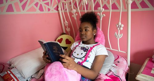A young woman sits in her bedroom and reads her scriptures