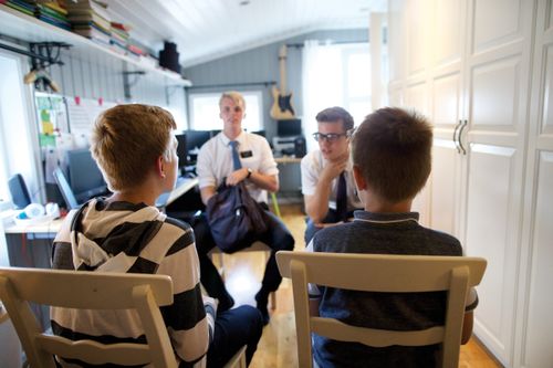 Two elder missionaries sit in a home and talk to two brothers.