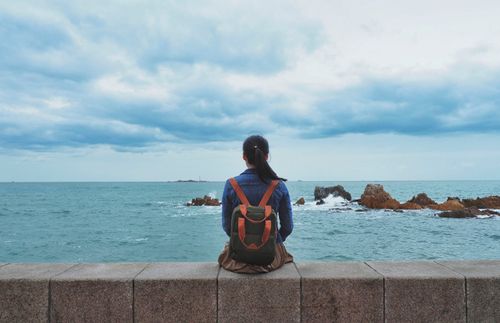 Girl sitting on ledge looking out into the ocean