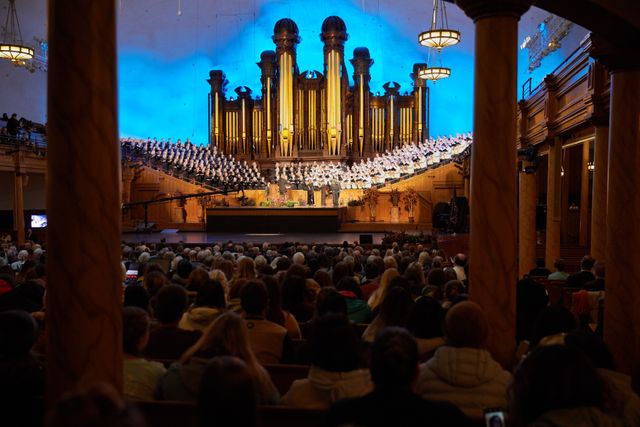 Audiences in the Salt Lake Tabernacle. Audiences sit on the pews. You can see the organ and a choir facing them.