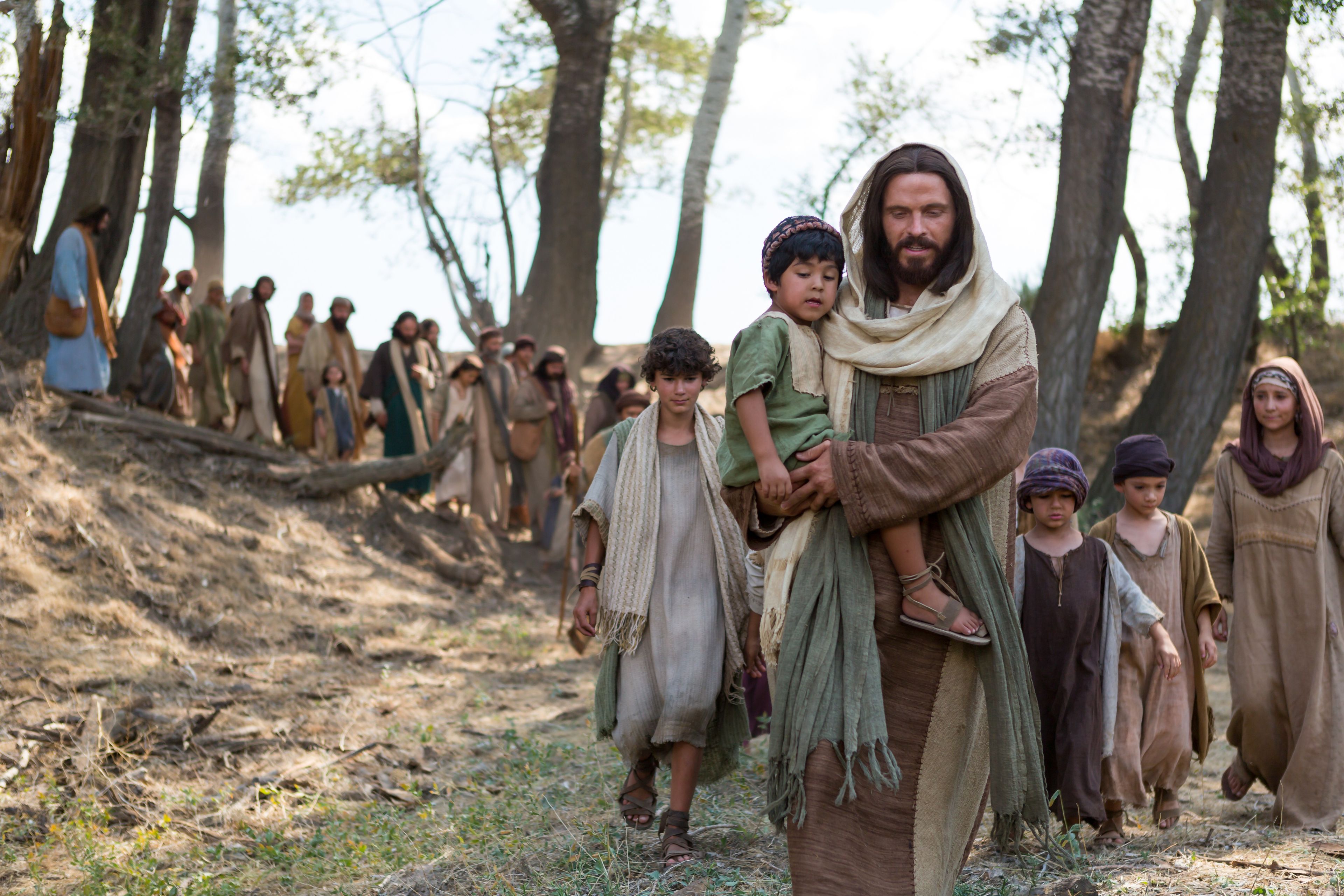 Cristo guía a un grupo de niños y a sus padres después de decir a Sus apóstoles: “Dejad a los niños venir a mí”.
