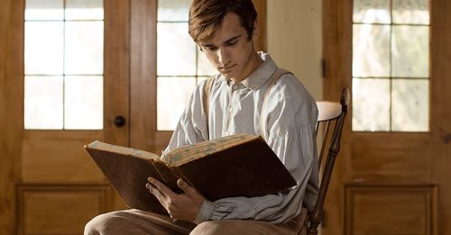 Young Joseph Smith sits in a chair reading the bible.