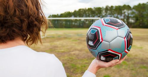 Back of young woman on soccer field, with soccer ball in hand, contemplating goal. (horiz)