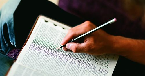 Manos de un joven sosteniendo lápiz rojo para marcar, mientras lee y estudia las Escrituras abiertas en su regazo. (Horizontal)