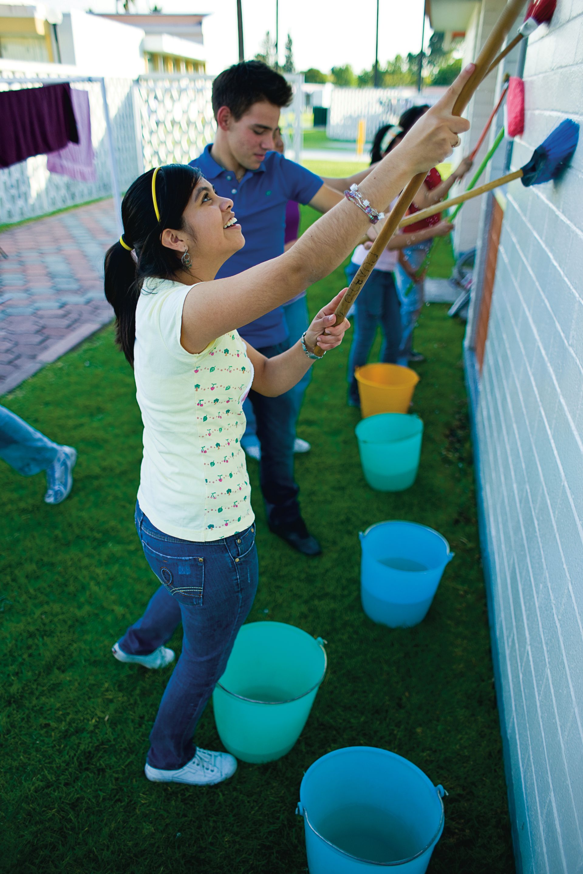 A group of youth clean white walls outside with brushes and water.
