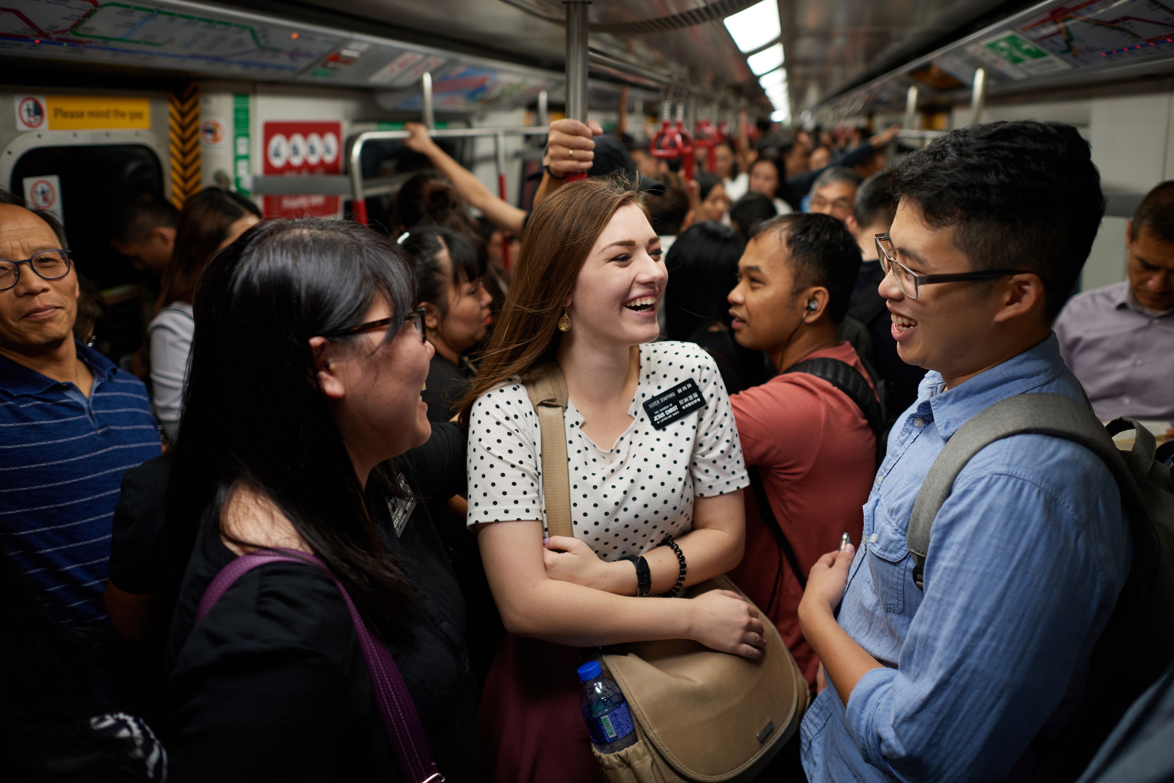 Two sister missionaries talking with a young man on a Hong Kong subway.