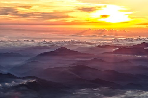 An aerial view of mountain peaks above low-lying clouds in Japan, with the sun rising in the background.