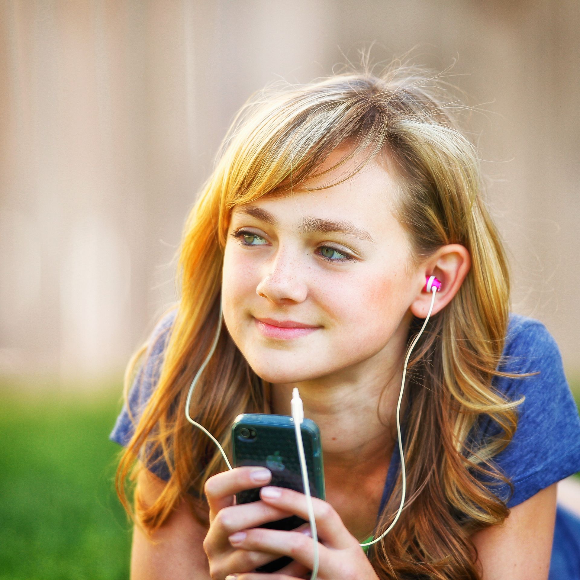A young woman lies on the grass, listening to music through earbuds.